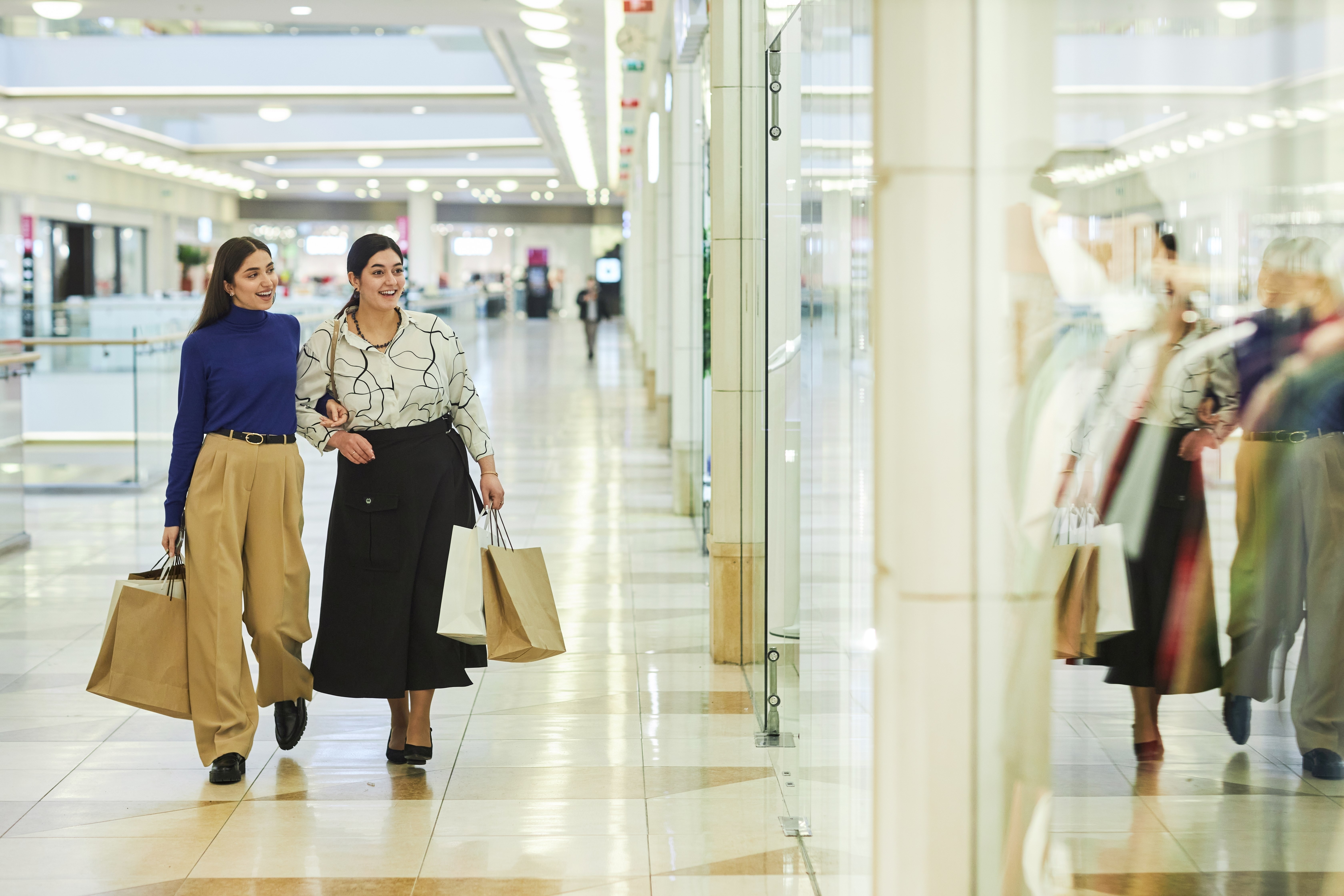 Two smiling women walking in shopping mall and looking at window displays copy space