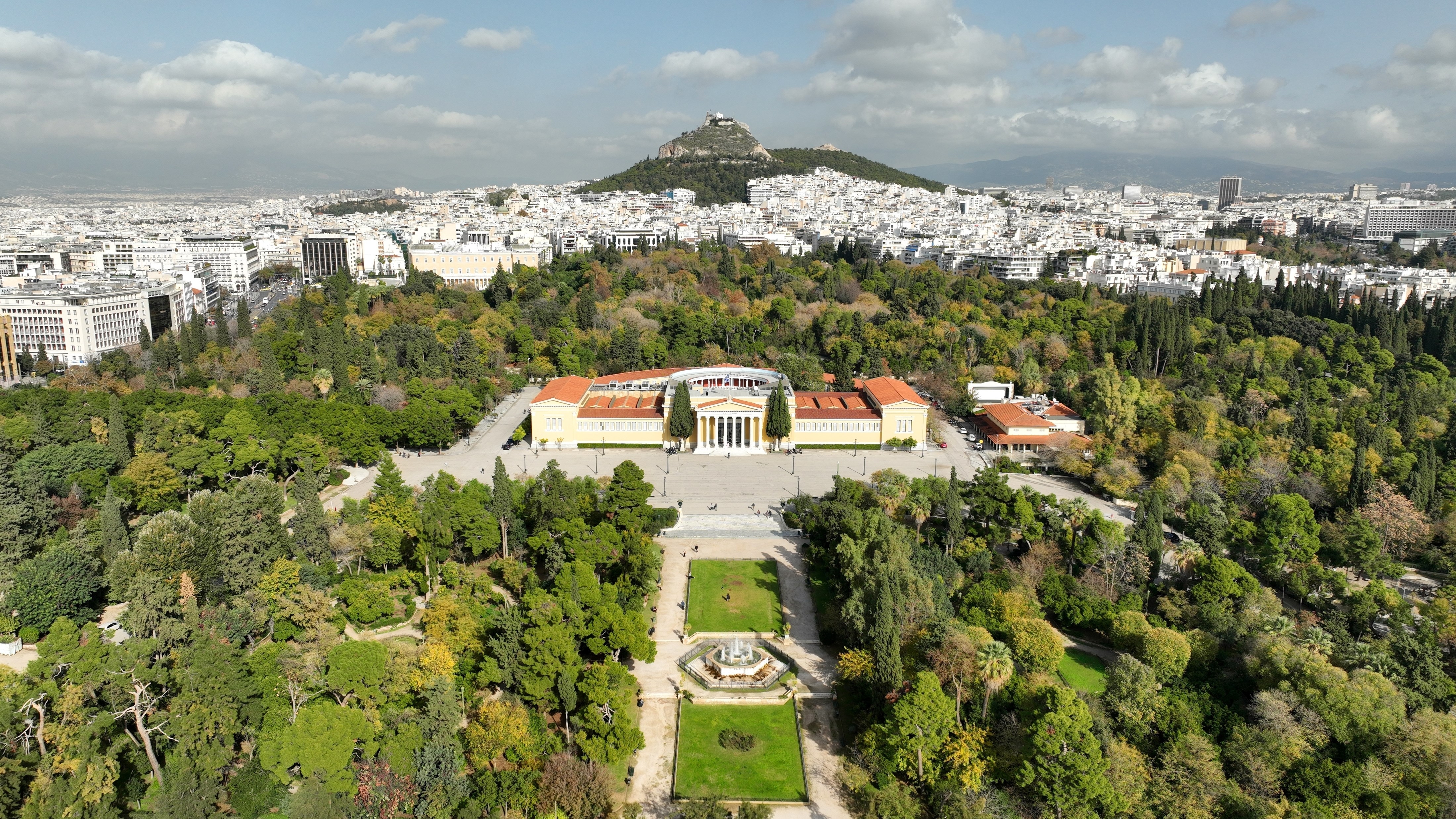 Aerial drone photo of renovated public neoclassic building of Zappeion used for events and meetings in the National Gardens of Athens and Lycabettus hill aligned at the background, Greece