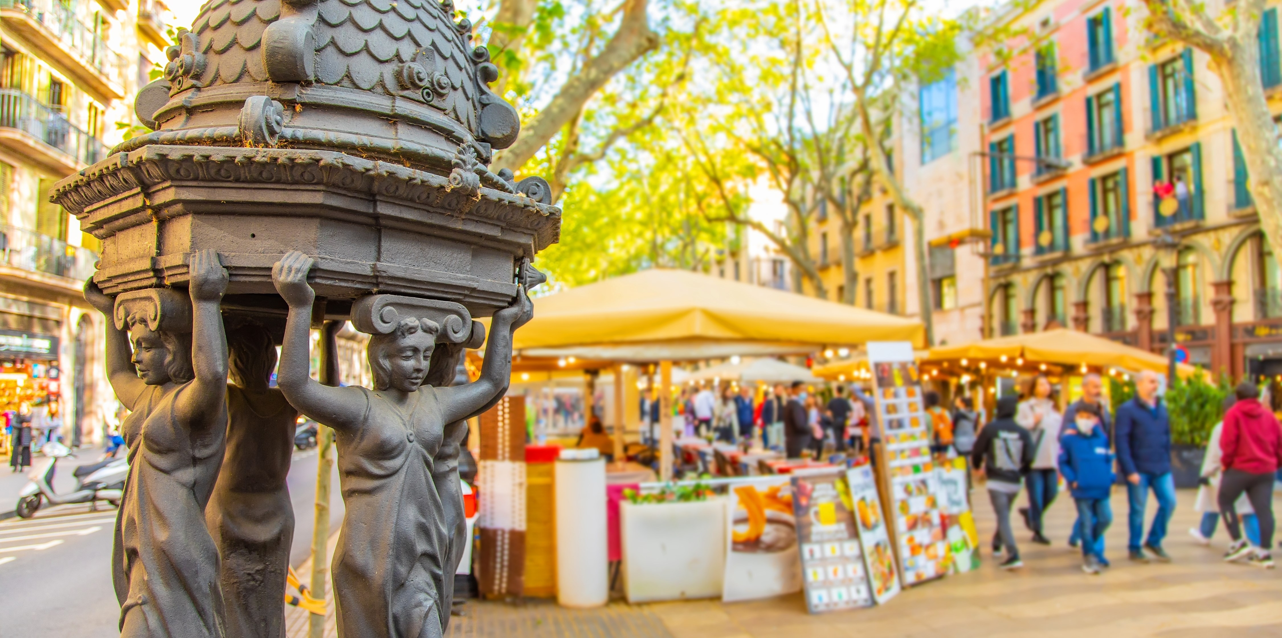 La Rambla pedestrian street in Barcelona city. Selective focus on drinking water fountain on foreground. La Rambla is popular tourist place in Barcelona, spanish travel photo.