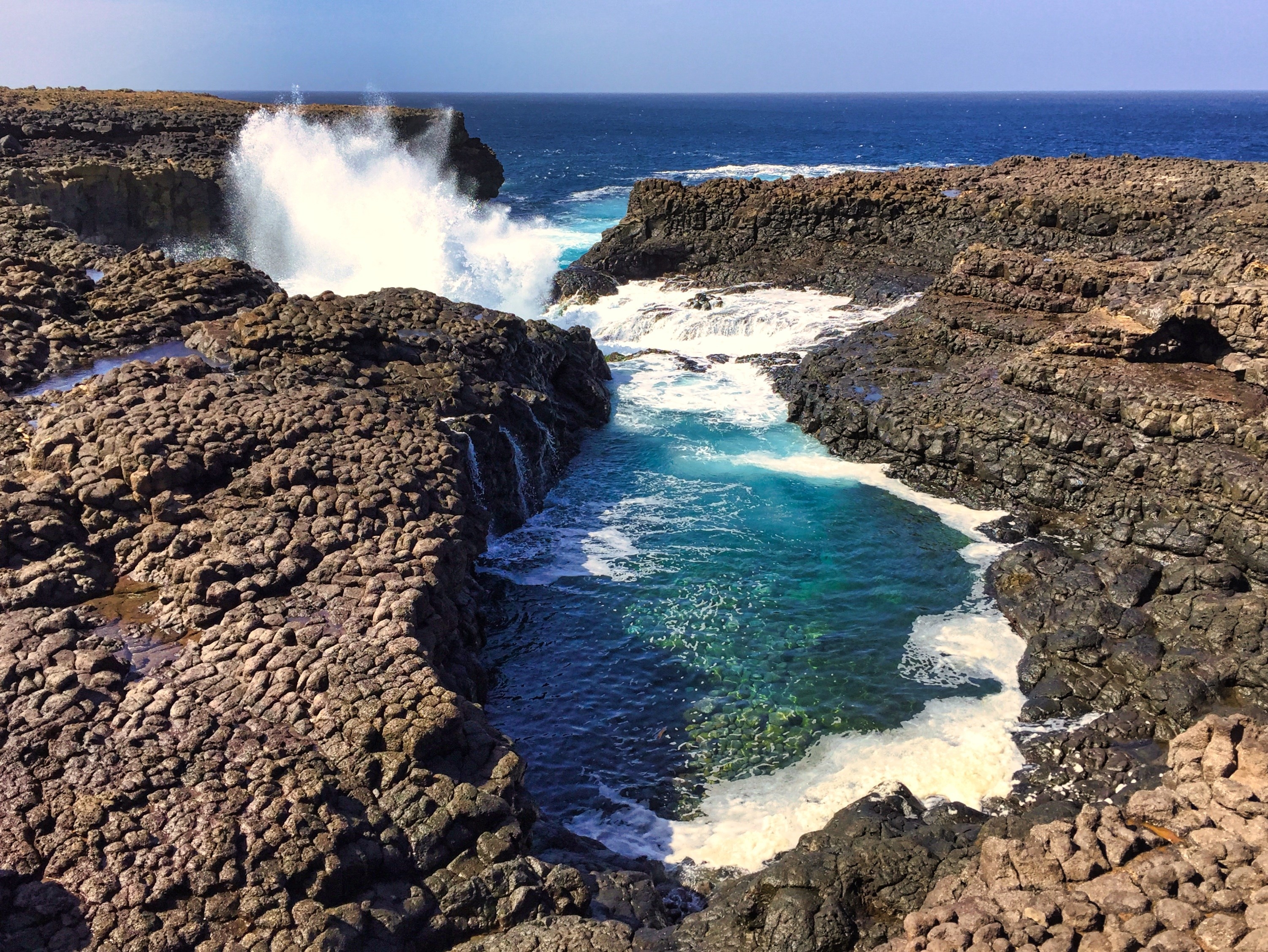 Buracona - The Blue Eye of Cabo Verde - blue lagoon inside a black rock with ocean splash in the back