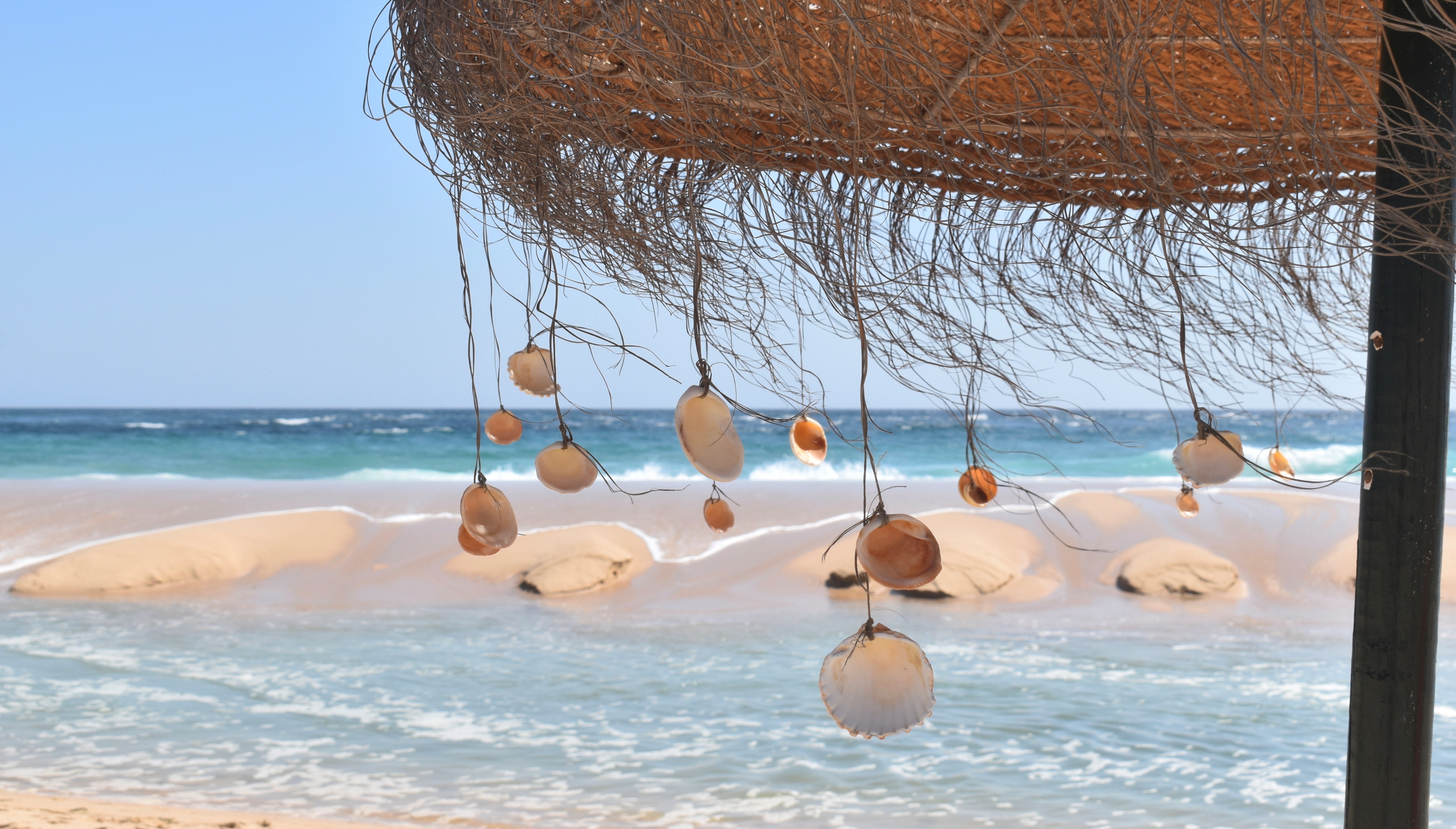 Beach life in the Algarve. Ilha Deserta. The ocean, the beach and an umbrela with seashells.