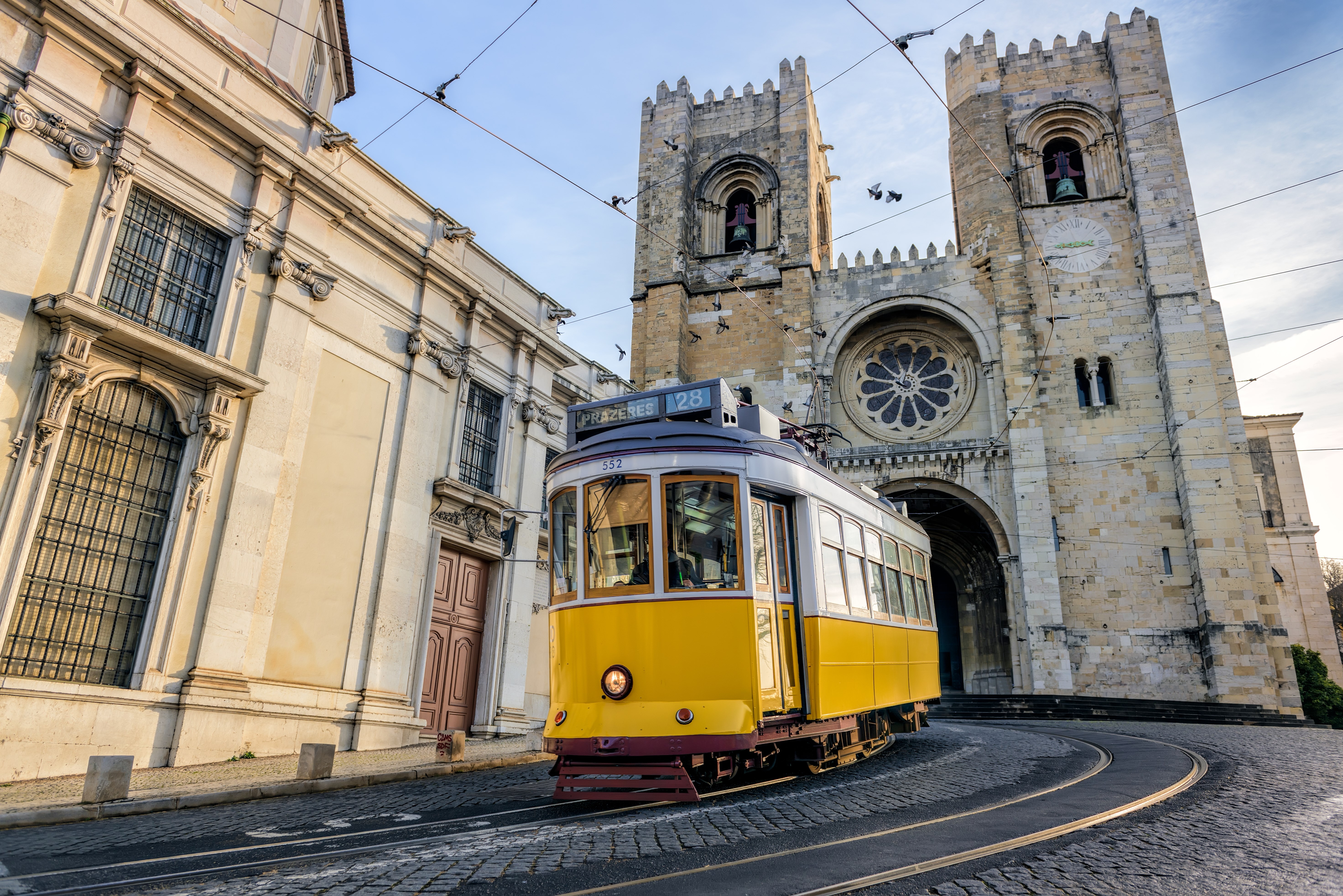 A famous yellow tram 28 passing in front of Santa Maria cathedral in Lisbon, Portugal