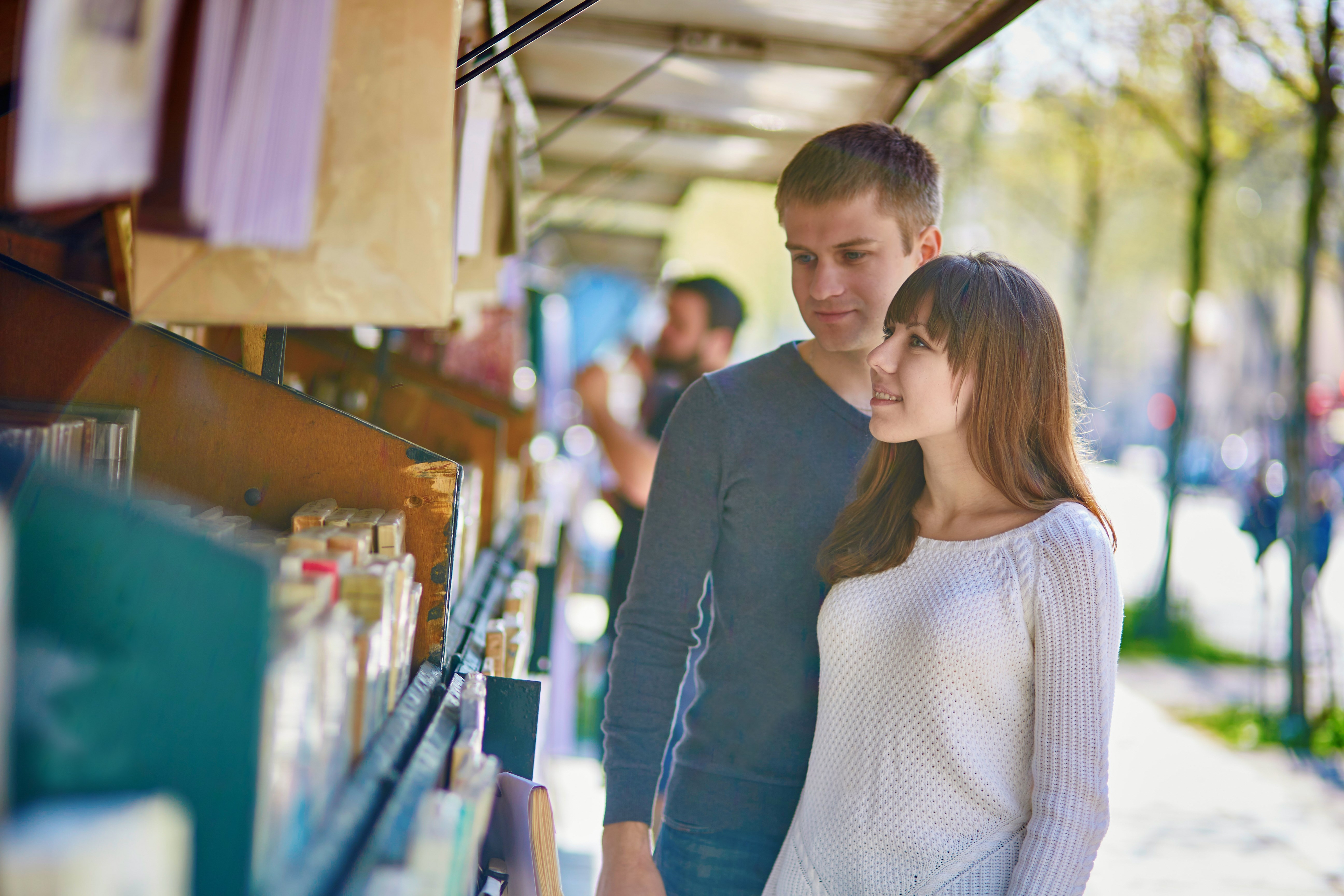 Romantic couple in Paris selecting a book from a bookseller near the Seine