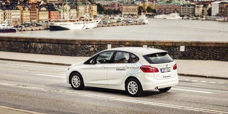 A white carsharing BMW from DriveNow with the silhouette of Old Town Stockholm behind A white carsharing BMW from DriveNow with the silhouette of Old Town Stockholm behind