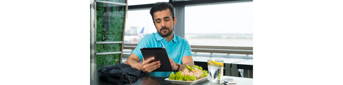 A man at a table, tablet in hand and a shrimp sandwich in front of him A man at a table, tablet in hand and a shrimp sandwich in front of him
