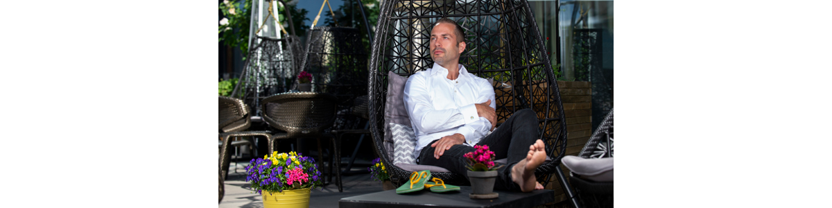 A man sitting in a hanging chair, feet on table and a pair of slippers beside A man sitting in a hanging chair, feet on table and a pair of slippers beside