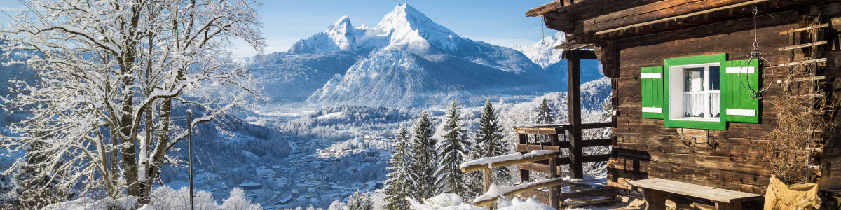 Panoramic view of scenic white winter wonderland mountain scenery in the Alps with traditional old wooden mountain chalets on a beautiful cold sunny day with blue sky and clouds Panoramic view of scenic white winter wonderland mountain scenery in the Alps with traditional old wooden mountain chalets on a beautiful cold sunny day with blue sky and clouds